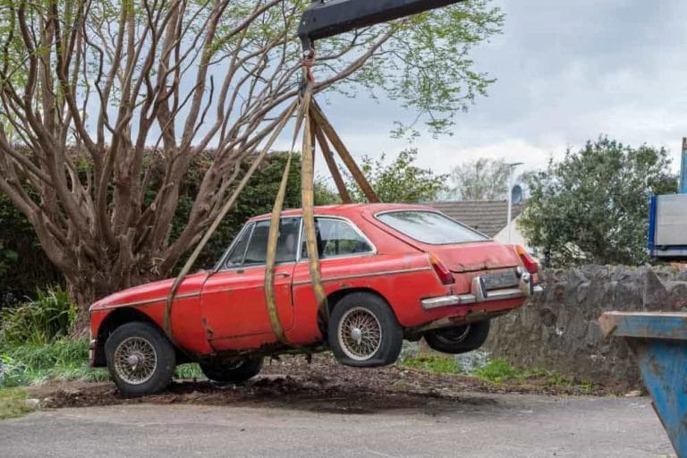 Old red car being lifted with straps for collection
