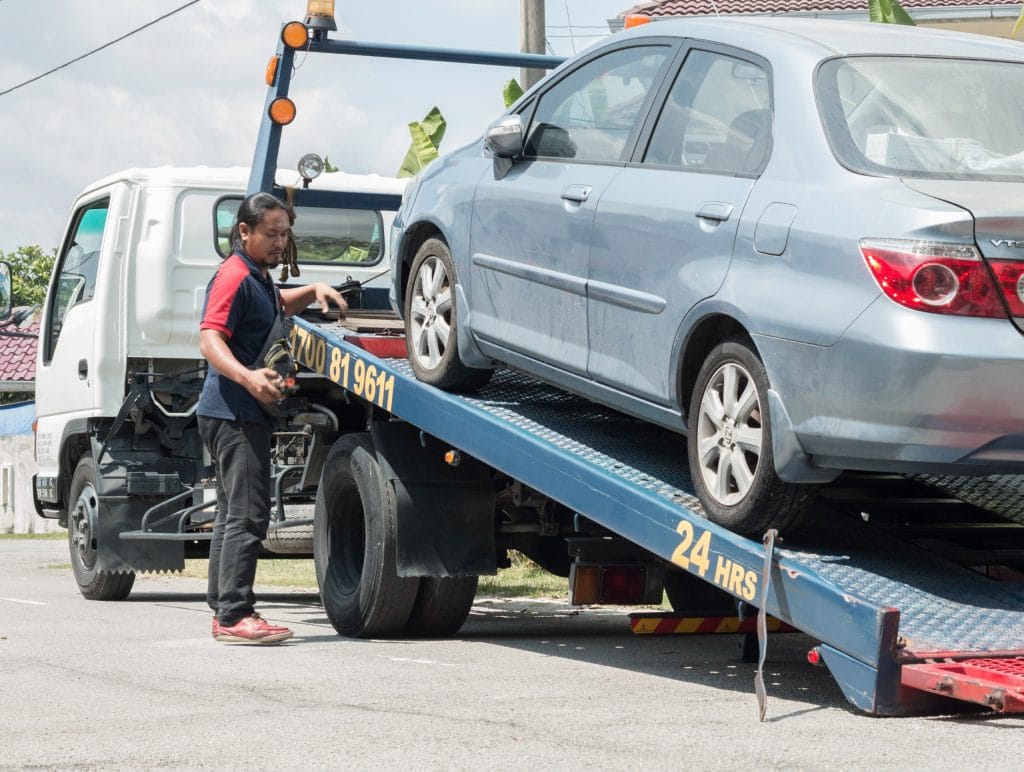 Old silver sedan loaded on a flatbed for scrap pickup