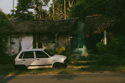 Unused white Maruti Zen parked outside an old shed