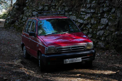 Old red Maruti 800 hatchback parked beside a stone wall